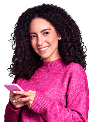 Mulher branca sorrindo de cabelos cacheados, vestindo uma blusa rosa e segurando o celular com a mão